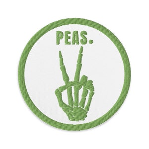Könnte beinhalten: Grüner gestickter Aufnäher mit einer Skeletthand, die ein Peace-Zeichen macht, und dem Wort "PEAS."