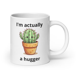 May include: White ceramic mug with a green cactus illustration and the text "I'm actually a hugger".
