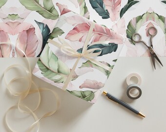 May include: A white gift wrap with a pink and green tropical leaf pattern. The gift wrap is wrapped around a box with a beige ribbon.