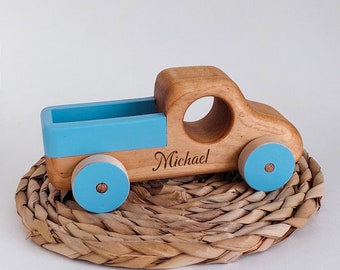 May include: A wooden toy truck with blue wheels and a blue bed. The truck is personalized with the name "Michael" engraved on the side.
