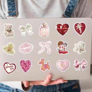 May include: A sheet of stickers featuring various designs, including hearts, bows, a teddy bear, a perfume bottle, a flower, lips, a cupid, an angel, a balloon animal, and a couple of hearts with text that says "Cinnamon Girl" and "Be mine".