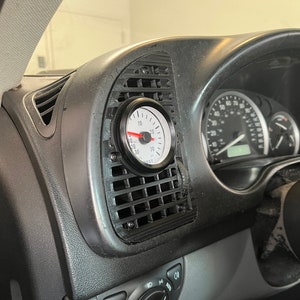 以下が含まれることがあります： 車のダッシュボードに、赤色の針が付いた白黒のブーストゲージが取り付けられています。ゲージは10 PSI を示しています。