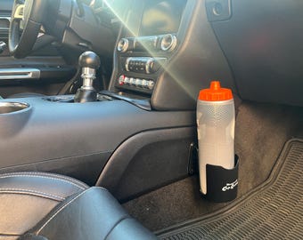 May include: A black car cup holder with the text "Car Cup Holder" on it. A clear water bottle with an orange lid is in the holder.