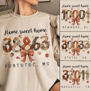 May include: A beige sweatshirt with the text "Home sweet home" and a postal code design. The postal code is decorated with a plaid pattern, a bow, and autumn leaves. Additional designs include postal codes for New York, Alabama, Atatal, Georgia, and Nashville, Tennessee.