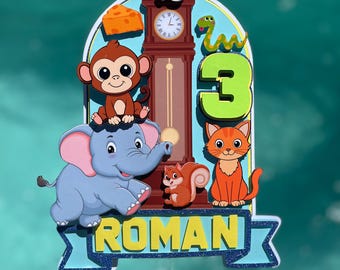 Könnte beinhalten: Ein mehrschichtiger Tortenaufleger mit einer braunen Standuhr, einem blauen Elefanten, einem braunen Affen, einer orangefarbenen Katze, einem Eichhörnchen, einer Maus, einer Schlange und einem Stück Käse. Die Zahl 3 ist grün und der Name ROMAN ist gelb.