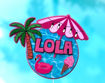May include: A pink and blue cake topper featuring a palm tree, an umbrella with fairy lights, a flamingo float, an ice cream cone, and the name "LOLA" in pink letters.