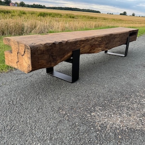 Può includere: Panca rustica in legno con finitura naturale. La panca è sostenuta da gambe in metallo nero. Il legno mostra venature e nodi visibili. La panca è lunga circa 244 cm.