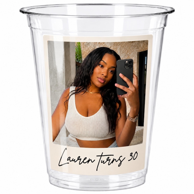 May include: A clear plastic disposable cup featuring a rectangular photo print of a person taking a selfie in a mirror. Below the photo, the text Lauren turns 30 is printed in a black script font on a light beige background.