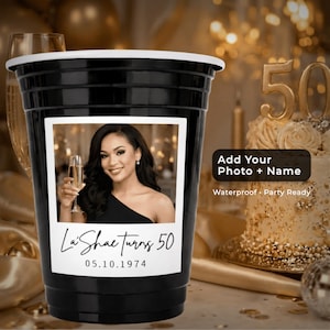 Può includere: Bicchiere da festa nero con bordo bianco e foto di una donna che tiene in mano un calice di champagne. La tazza riporta la scritta "La'Shae turns 50" e "05.10.1974". È visibile anche il testo "Add Your Photo + Name".
