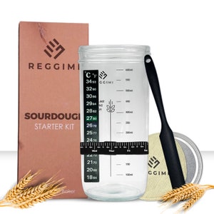 May include: A sourdough starter kit with a clear glass jar, a black stirring spoon, a beige cloth, and a brown box with the text "REGGIMI SOURDOUGH STARTER KIT" and a wheat stalk graphic. The jar has a temperature gauge and markings in Celsius and Fahrenheit, and milliliters.