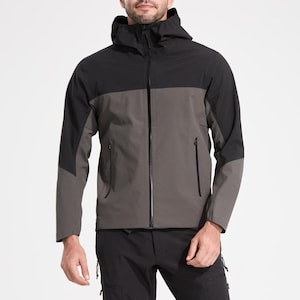 May include: A black and grey hooded jacket with a zip fastening. The jacket has a colour block design with a grey body and black sleeves. The model is wearing black trousers and brown shoes.