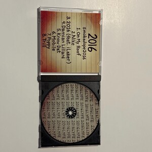 May include: A clear plastic CD case, open to reveal a CD and track listing. The CD case has the title "2016" and the artist name "Smokedope2016". The track list includes songs like "On My Roof" and "Nike".