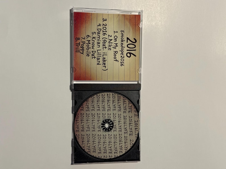 May include: A clear plastic CD case, open to reveal a CD and track listing. The CD case has the title "2016" and the artist name "Smokedope2016". The track list includes songs like "On My Roof" and "Nike".