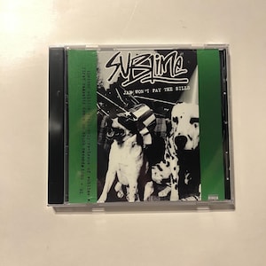 May include: A CD case featuring the band Sublime's album "Jah Won't Pay the Bills." The cover art displays a black and white image of two dogs. The album title and band name are in white text.