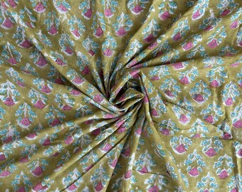 May include: Close-up of a folded fabric with a repeating floral pattern. The fabric has a mustard yellow background with pink, white, and teal floral designs. The fabric is bunched up in the center, creating shadows and texture.