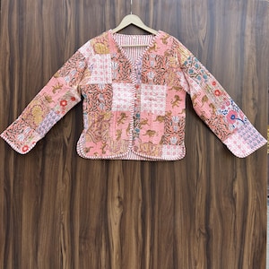 May include: A patchwork jacket with a V-neck and long sleeves. The jacket features a mix of floral and animal print patterns in shades of pink, peach, and brown. It has a button-up front and a striped lining.