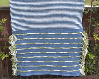May include: A blue and white striped throw rug with green stripes at the bottom. The rug has fringe on all sides.