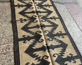 May include: A black and beige patterned rug with a geometric design. The rug is made of natural fibers and has a rustic look.