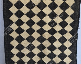 May include: Black and cream checkered rug with a diamond pattern. The rug is made of natural fibers and has a fringed edge.