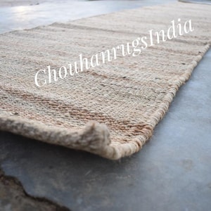 Può includere: Un tappeto in fibra naturale realizzato in juta, un materiale sostenibile e resistente. Il tappeto ha un colore marrone chiaro e una trama tessuta. Il tappeto è perfetto per aggiungere un tocco di bellezza naturale a qualsiasi stanza.