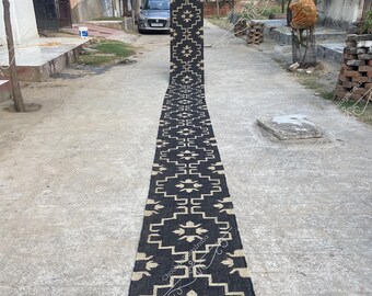 May include: A black and white geometric patterned runner rug with a fringe edge. The rug is laid out on a gray concrete surface.