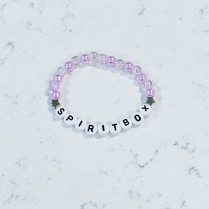 May include: A pink and white beaded bracelet with the word "SPIRITBOX" spelled out in black letters on white beads.