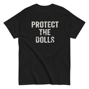 Può includere: Maglietta nera con testo bianco che recita "PROTECT THE DOLLS".
