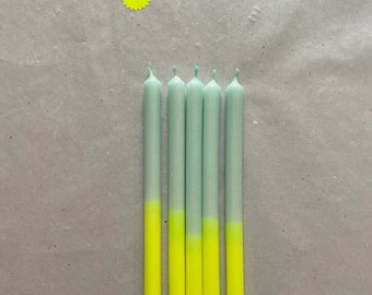 Könnte beinhalten: Fünf mintgrüne Kerzen mit neon-gelb getauchten Spitzen. Ein kleiner gelber sternförmiger Aufkleber befindet sich in der oberen linken Ecke. Die Kerzen sind vertikal auf einer hellgrauen Oberfläche angeordnet.