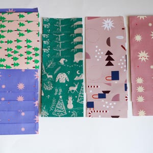Può includere: Una collezione di fogli di carta da regalo piegati con vari disegni festivi. I motivi includono alberi di Natale verdi su rosa, stelle blu, scene invernali verdi, forme geometriche rosa e scoppi di stelle rosa. Ideale per confezionare regali.