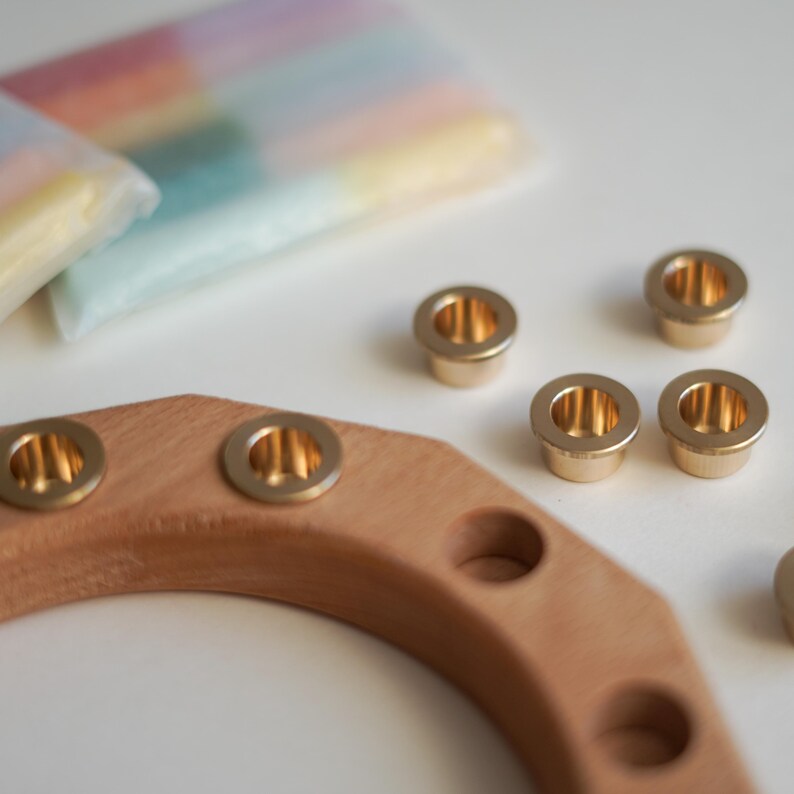 May include: A wooden candle holder with brass-colored metal inserts. Several loose metal inserts are scattered around the holder. Pastel-colored candles are visible in the background, suggesting a home decor theme.