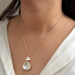 Puede incluir: Un collar de cadena de oro con un colgante en forma de l&aacute;grima que presenta una gran piedra preciosa transparente rodeada de piedras preciosas transparentes m&aacute;s peque&ntilde;as.