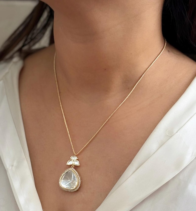 Puede incluir: Un collar de cadena de oro con un colgante en forma de l&aacute;grima que presenta una gran piedra preciosa transparente rodeada de piedras preciosas transparentes m&aacute;s peque&ntilde;as.