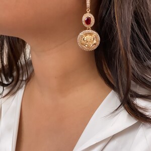 May include: Gold tone drop earrings with a red stone and a circular pendant featuring a detailed design.