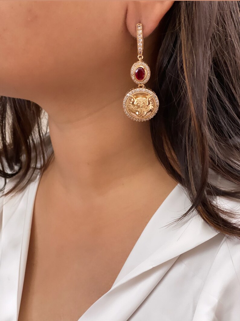 May include: Gold tone drop earrings with a red stone and a circular pendant featuring a detailed design.
