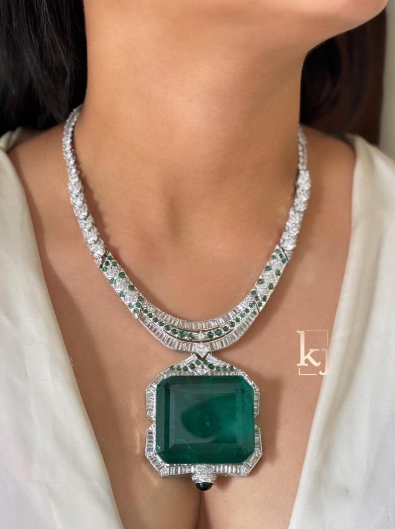 May include: A dazzling necklace featuring a large, emerald-cut green gemstone pendant. The necklace is adorned with sparkling white and green gemstones set in a silver-toned metal, creating a luxurious and elegant design.