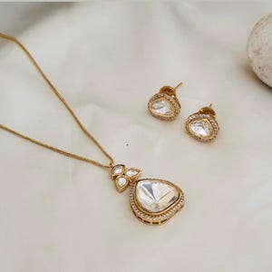 Puede incluir: Un collar de oro con un colgante en forma de l&aacute;grima engastado con piedras transparentes. El colgante est&aacute; rodeado de piedras m&aacute;s peque&ntilde;as. El collar viene con un par de pendientes a juego.
