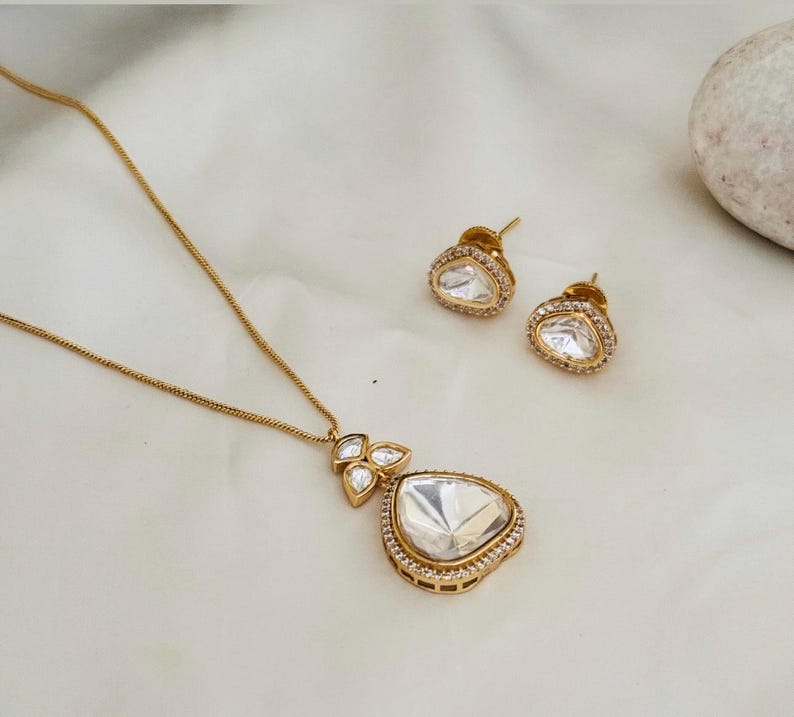 Puede incluir: Un collar de oro con un colgante en forma de l&aacute;grima engastado con piedras transparentes. El colgante est&aacute; rodeado de piedras m&aacute;s peque&ntilde;as. El collar viene con un par de pendientes a juego.