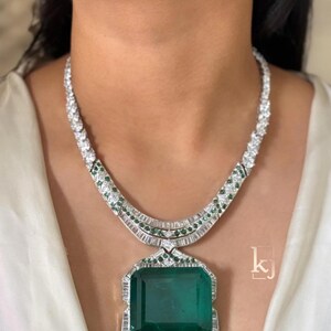 May include: A dazzling necklace featuring a large, rectangular emerald pendant. The pendant is surrounded by a halo of sparkling diamonds. The necklace has a white gold or platinum chain with diamond and emerald accents, creating a luxurious look.