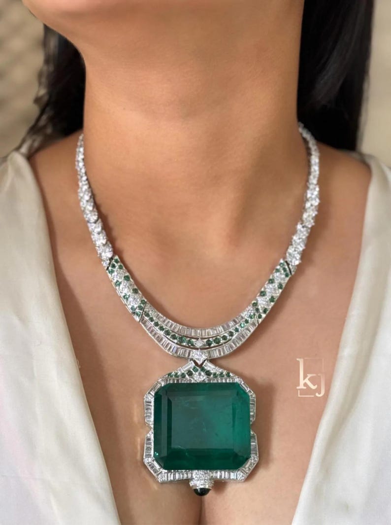 May include: A dazzling necklace featuring a large, rectangular emerald pendant. The pendant is surrounded by a halo of sparkling diamonds. The necklace has a white gold or platinum chain with diamond and emerald accents, creating a luxurious look.
