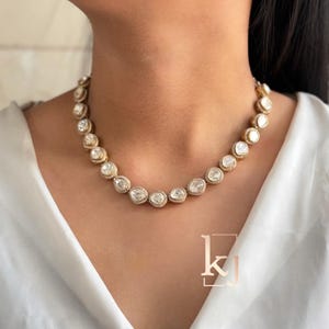 Könnte beinhalten: Eine goldene Halskette mit einer Reihe großer, runder, klarer Steine, die in einen goldenen Rahmen gefasst sind. Die Steine sind von kleineren, klaren Steinen umgeben.