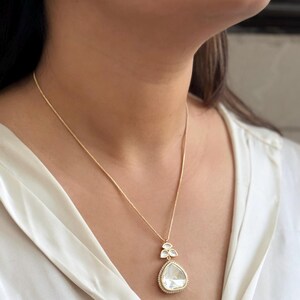 Puede incluir: Un collar de cadena de oro con un colgante en forma de l&aacute;grima que presenta una gran piedra preciosa transparente rodeada de piedras preciosas transparentes m&aacute;s peque&ntilde;as.
