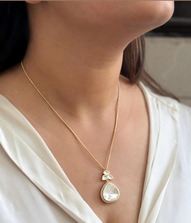 Puede incluir: Un collar de cadena de oro con un colgante en forma de l&aacute;grima que presenta una gran piedra preciosa transparente rodeada de piedras preciosas transparentes m&aacute;s peque&ntilde;as.