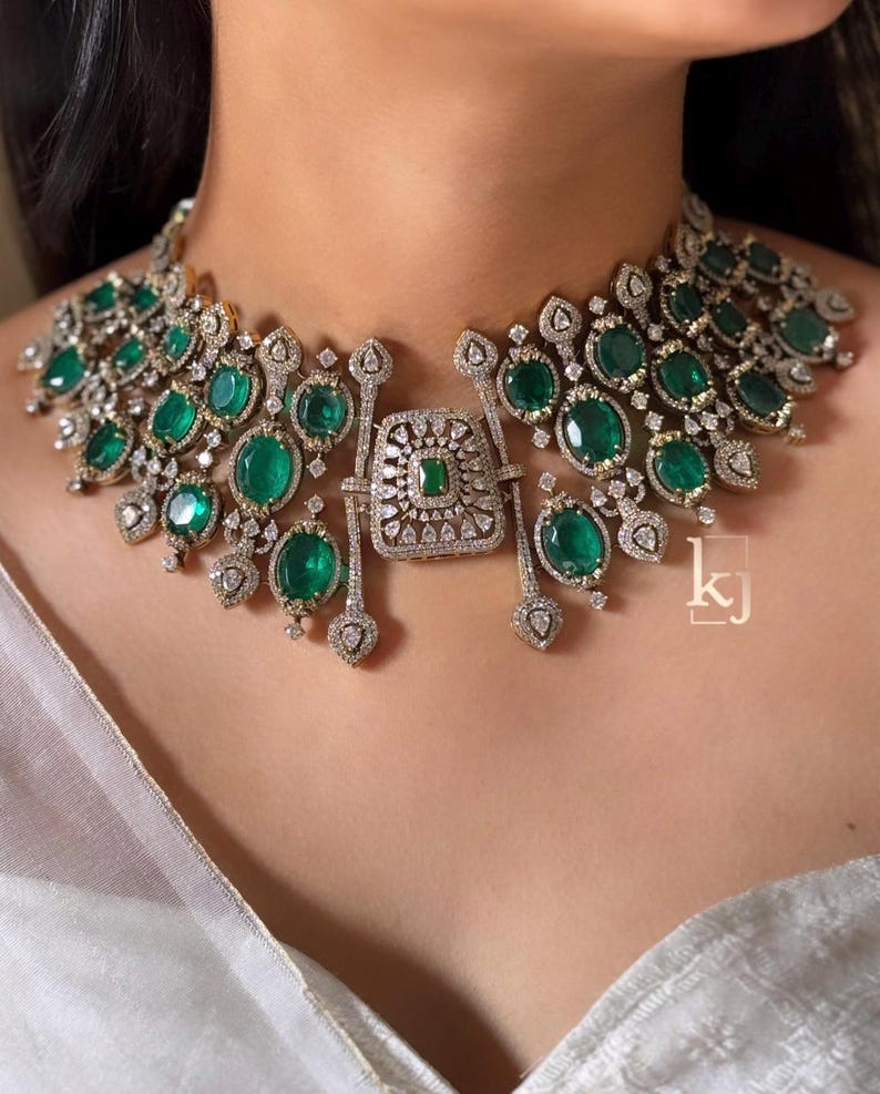 May include: A statement necklace featuring numerous oval-cut green gemstones set in silver-toned metal, accented with small clear pav&eacute; stones. The centerpiece is a rectangular plaque with a central green stone, surrounded by intricate metalwork.