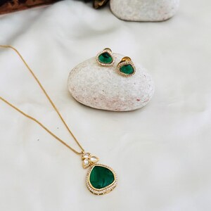 Puede incluir: Un collar de oro con un colgante de piedra preciosa verde y pendientes a juego. El colgante est&aacute; rodeado de piedras preciosas transparentes m&aacute;s peque&ntilde;as.