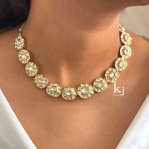 May include: A gold-toned necklace featuring circular, clear gemstones set in a gold frame. The necklace is composed of multiple circular elements, creating a continuous design. The necklace is worn around the neck.