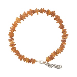 Puede incluir: Un collar hecho de cuentas de color ámbar, de forma irregular. Las cuentas están ensartadas, formando una forma circular. El collar tiene un cierre y una cadena de color plateado.