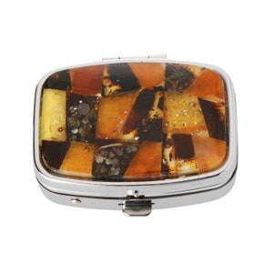 May include: A silver pill box with a hinged lid. The lid is decorated with a mosaic of amber stones in shades of brown, yellow, and orange.