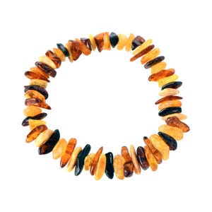 Puede incluir: Un brazalete hecho de cuentas de ámbar de forma irregular en tonos amarillos, naranjas y marrones. Las cuentas están ensartadas para formar una forma circular. El fondo es blanco.