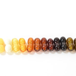 May include: A row of amber beads in various shades of yellow, orange, brown, and black. The beads are arranged in a gradient from light to dark.