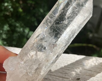 May include: A clear quartz crystal point with a double termination. The crystal is approximately 12.5 cm long and has a natural, raw appearance.